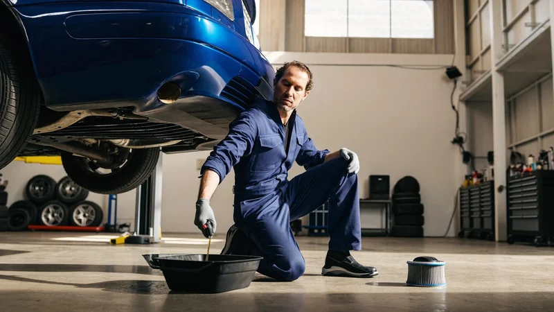 Mekaniker tapper motorolie fra en hævet personbil ved siden af nyt oliefilter